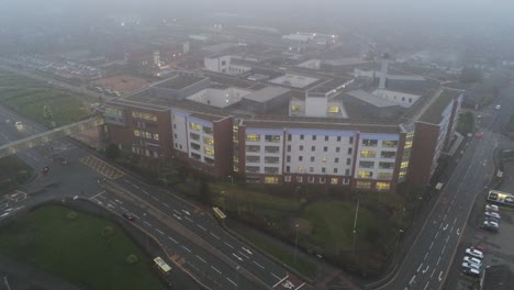 Misty-foggy-hospital-building-UK-town-traffic-aerial-view-descent-tilt-up