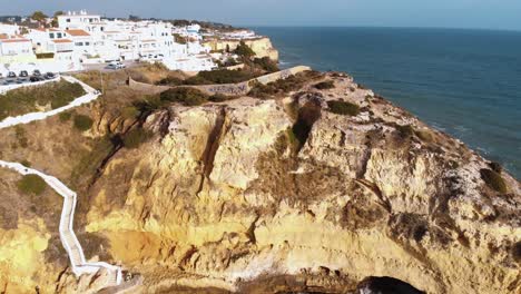 Panoramic-view-of-Paradise-Beach,-cliffs-and-downhill-path-in-Carvoeiro---Aerial-Panoramic-reveal-shot