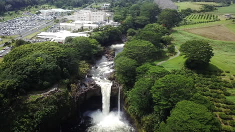 Aerial-of-Rainbow-Falls-and-surrounding-nature-and-buildings,-Hawaii