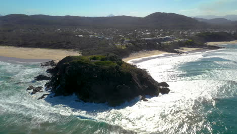Wide-rotating-drone-shot-of-coastline,-small-town-and-rock-outcropping-at-Cabarita-Beach-Australia