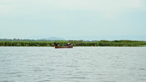 Fisherman-in-a-boat-drawing-his-net-for-fish-at-Boraphet-Lake-in-Nakhon-Sawan,-Thailand