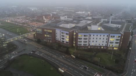 Aerial-view-British-NHS-hospital-on-misty-wet-damp-morning-high-slow-orbit-right