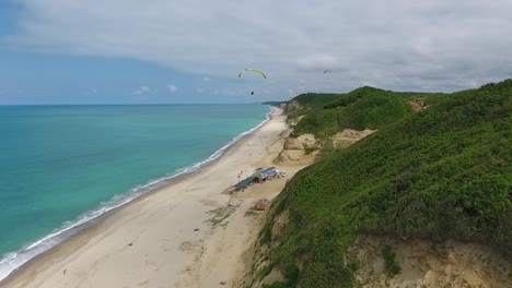 Paraglider-Flies-Over-Beach-Near-Hills-Drone-Follow