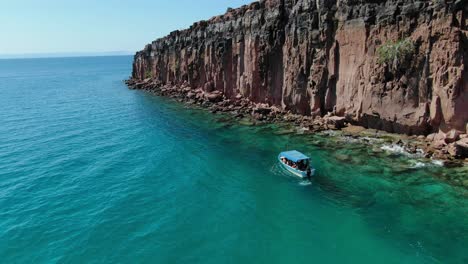 Aerial-view-moves-away-shot,-a-tourist-boat-park-beside-the-Isla-Espiritu-Santo-in-Baja-Sur,-Mexico,-scenic-view-of-the-emerald-green-sea-on-a-bright-sunny-day
