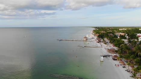 Beweglicher-Schuss-Der-Luftaufnahme,-Malerischer-Strand-Von-Isla-Holbox-In-Mexiko,-Leute,-Die-Um-Den-Strand-An-Einem-Hellen-Sonnigen-Tag-Schwimmen,-Klarer-Blauer-Himmel-Im-Hintergrund
