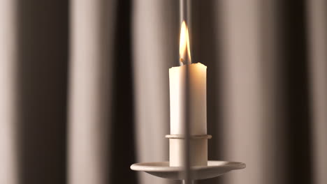 Soft-candle-burns-in-front-of-drapes,-close-up-bokeh-slider-shot