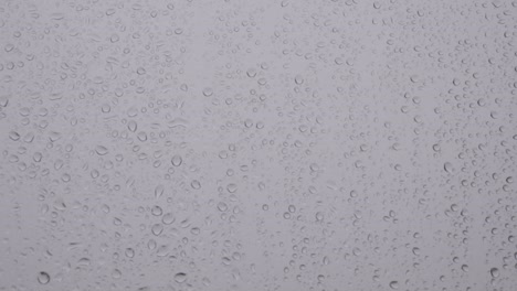 Droplets-of-rain-slowly-roll-down-window-pane,-Static-Closeup-Background