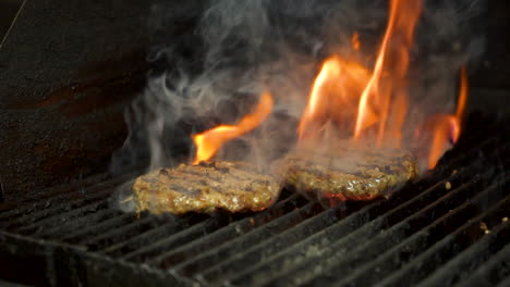 Burger-patty-grilled-over-flame,-fire-and-smoke-flare-up-around-hamburger-meat,-slide-slow-motion