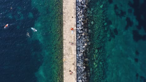 Amazing-pier-on-rocky-stone-Mediterranean-turquoise-coastline,-aerial-top-down