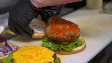 Cook-places-top-bun-on-buffalo-chicken-sandwich-and-cheeseburger,-close-up-slow-motion-slide-HD