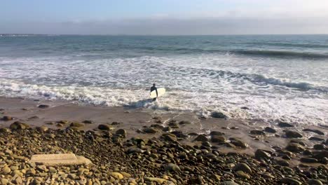 A-surfer-paddles-out-into-the-Pacific-Ocean-in-Ventura,-California