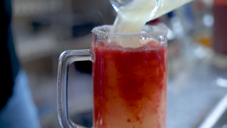 Bartender-pours-frozen-margarita-over-strawberry-puree-in-beer-mug,-slow-motion-HD