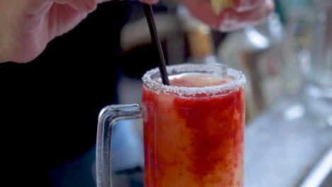 Bartender-garnishes-frozen-strawberry-margarita,-woman-finished-cocktail-with-straw-and-lime-wedge,-slow-motion-4K