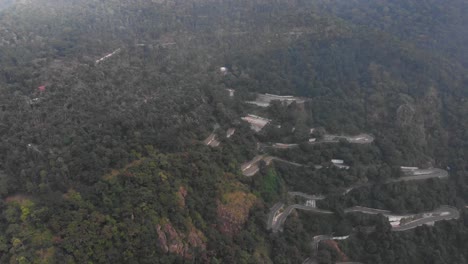 Yercaud-highway-hairpin-bend-covered-with-thick-lush-of-trees-and-vehicles-are-passing-in-the-highway-drone-shot