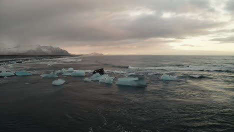 Volando-Hacia-Un-Iceberg-Flotante-Con-Olas-Rompiendo-En-La-Playa-De-Diamantes-En-El-Sur-De-Islandia