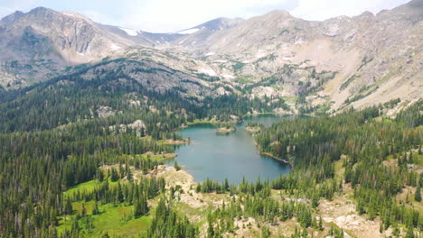 Aerial-Drone-Footage-of-Beautiful-Rocky-Mountain-Lake-with-Clear-Blue-Water-Surrounded-by-Mountain-Peaks-and-Thick-Pine-Tree-Forest-in-Nederland-Colorado