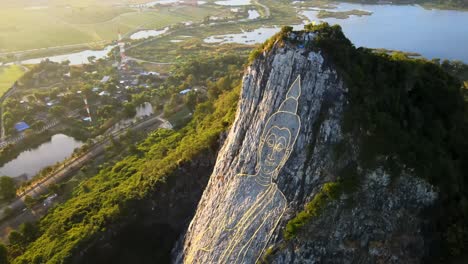 4k-Top-down-Aerial-pan-above-carved-Buddha-Image-made-from-Gold-on-a-cliff-at-Khao-Chee-Chan,-Pattaya,-Thailand
