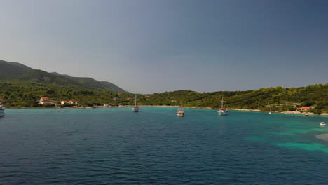 Sailboats-anchored-off-Mediterranean-Sea-Croatia-coastline,-aerial-dolly-view