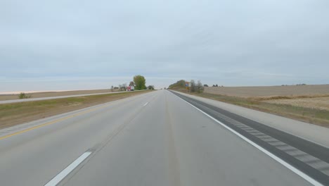 POV-driving-on-a-divided-highway-empty,-harvested-fields-on-a-cloudy-winter-day-in-rural-eastern-lowa