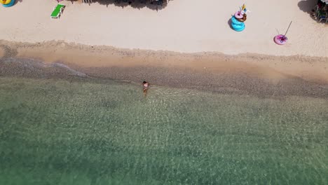 4k-aerial-drone-footage-of-a-lone-beach-babe-relaxing-in-the-beautiful-coastal-waves-of-a-deserted-resort-in-Ko-Larn-Island,-Thailand