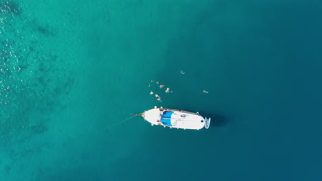 People-swimming-in-sea-beside-luxury-yacht,-aerial-top-down-view