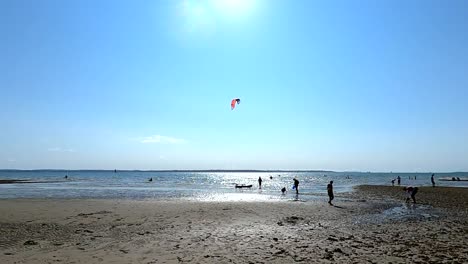 Eine-Strandszene-Im-Sommer-Mit-Passanten-Und-Kitesurfern-Im-Wasser
