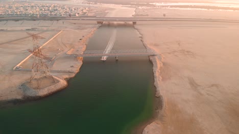Abu-Dhabi,-Aerial-view-of-jetski-passing-under-metal-bridge-at-sunset