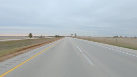 POV-driving-on-a-interstate-highway-past-flat,-harvested-fields-on-a-cloudy-winter-day-in-rural-western-Illinois