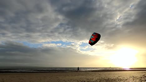 A-man-flying-a-power-kite-quickly-through-the-air-in-figures-of-8-on-a-beach-during-sunset