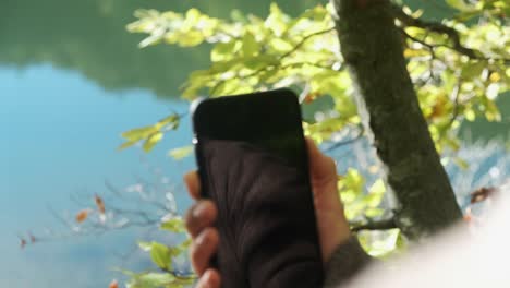 Woman's-Finger-Turn-Off-Cellphone-In-Forest-With-Calm-Lake-In-Background