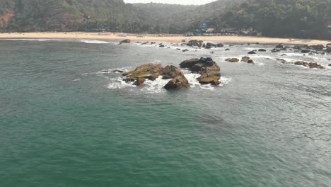 Coastal-eroded-rocks-near-shoreline-in-Arambol,-in-Goa,-India---Aerial-Crane-down-tilt-up-reveal