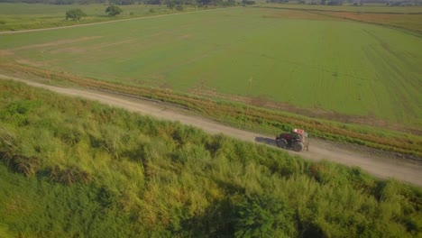 Aerial-shot-of-a-tractor-going-on-a-dirt-road-across-the-countryside