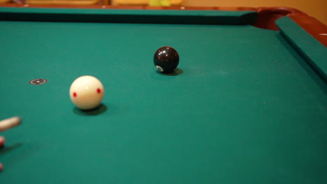 Slow-Motion-Billiards-Person-Shooting-solid-black-8-ball-in-corner-pocket-on-a-pool-table-with-green-felt-using-the-cue-ball-and-back-spin-or-draw-after-practice-strokes-with-cue-stick-Close-Up