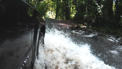 Action-shot-of-car-driving-through-water-on-road-in-jungle,-Hawaii