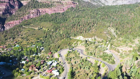 Aerial-Drone-Lowering-Motion-of-Beautiful-Ouray-Colorado-Pine-Tree-Forest-and-Mountain-Cliffs-with-Cars-Driving-on-Highway-550-by-Rocky-Mountain-Houses