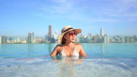 Asiatische-Frau-Mit-Großer-Sonnenbrille-Und-Hut,-Die-Sich-Im-Infinity-Pool-Entspannt