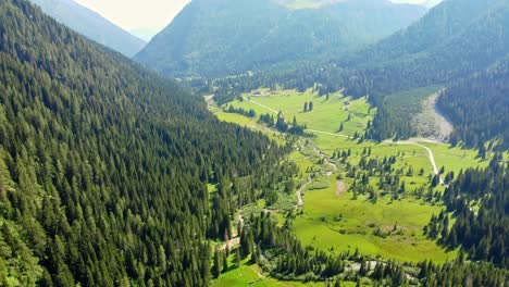 flying-over-a-beautiful-valley-in-northern-italy,-high-in-the-mountains-green-healthy-grass-stretches-from-one-side-to-the-other,-a-small-river-flows-in-the-middle