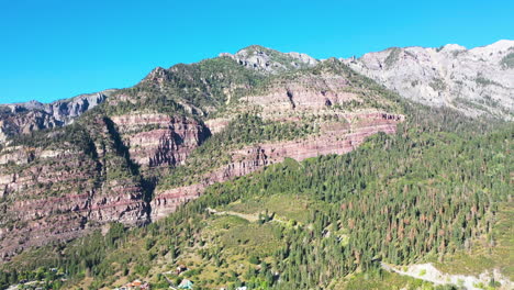 Aerial-Drone-Pan-Left-of-Beautiful-Ouray-Colorado-Thick-Pine-Tree-Forest-and-Mountain-Range-During-Summer-with-Rocky-Mountain-Town-Houses-and-Cars-Driving