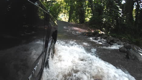 Car-driving-through-water-on-flooded-asphalt-road-in-Hawaii-jungle,-slowmotion