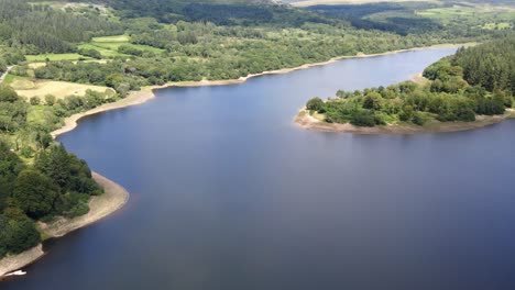 Flying-over-tranquil-woodland-lake-in-Dartmoor-National-Park,-Devon,-UK
