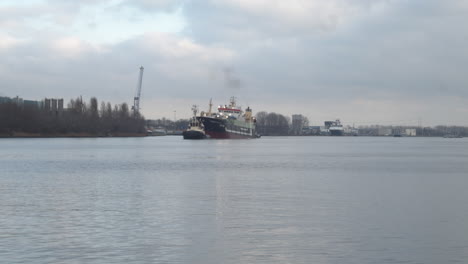 medium-shot-of-Tug-boat-guiding-large-ship-over-river