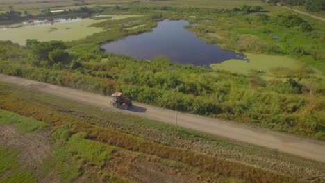 Drone-shot-of-a-tractor-going-on-a-dirt-road-across-the-countryside