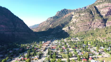 Aerial-Drone-Lowering-Motion-of-Ouray-Colorado-Mountain-Town,-Cars-Driving-Through-City-and-Houses-Surrounded-by-Rocky-Mountain-Cliffs-and-Pine-Tree-For