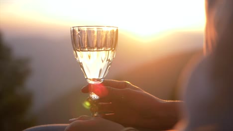 young-woman-holds-champagne-glass-in-hands-at-fiery-sunset,-slow-motion-closeup