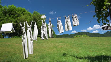Vintage-Clothing-Hanging-Outside-Against-Green-Field-And-Blue-Sky-With-White-Clouds-Background-On-A-Sunny-Day---Static-Shot