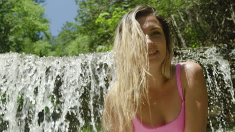 Cute-fun-young-woman-smiles-and-poses-in-front-of-a-waterfall-in-a-forest-nature-setting