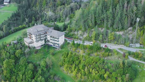 Drone-view-of-a-building-on-a-hill-with-trees-and-mountains-surround-it