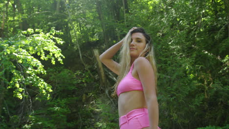 Hot-young-woman-poses-and-smiles,-standing-in-a-river-surrounded-by-forest