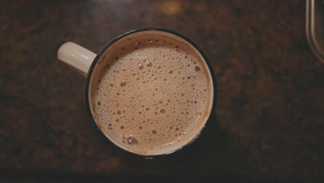 Cup-Of-Hot-Frothy-Chocolate-Drink-On-Kitchen-Table-For-Breakfast---top-shot