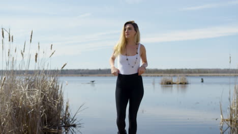Confident-trendy-young-woman-walks-towards-the-camera,-lake-in-the-background